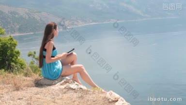 年轻的白人妇女在海边的山顶上用电子阅读器阅读电子书